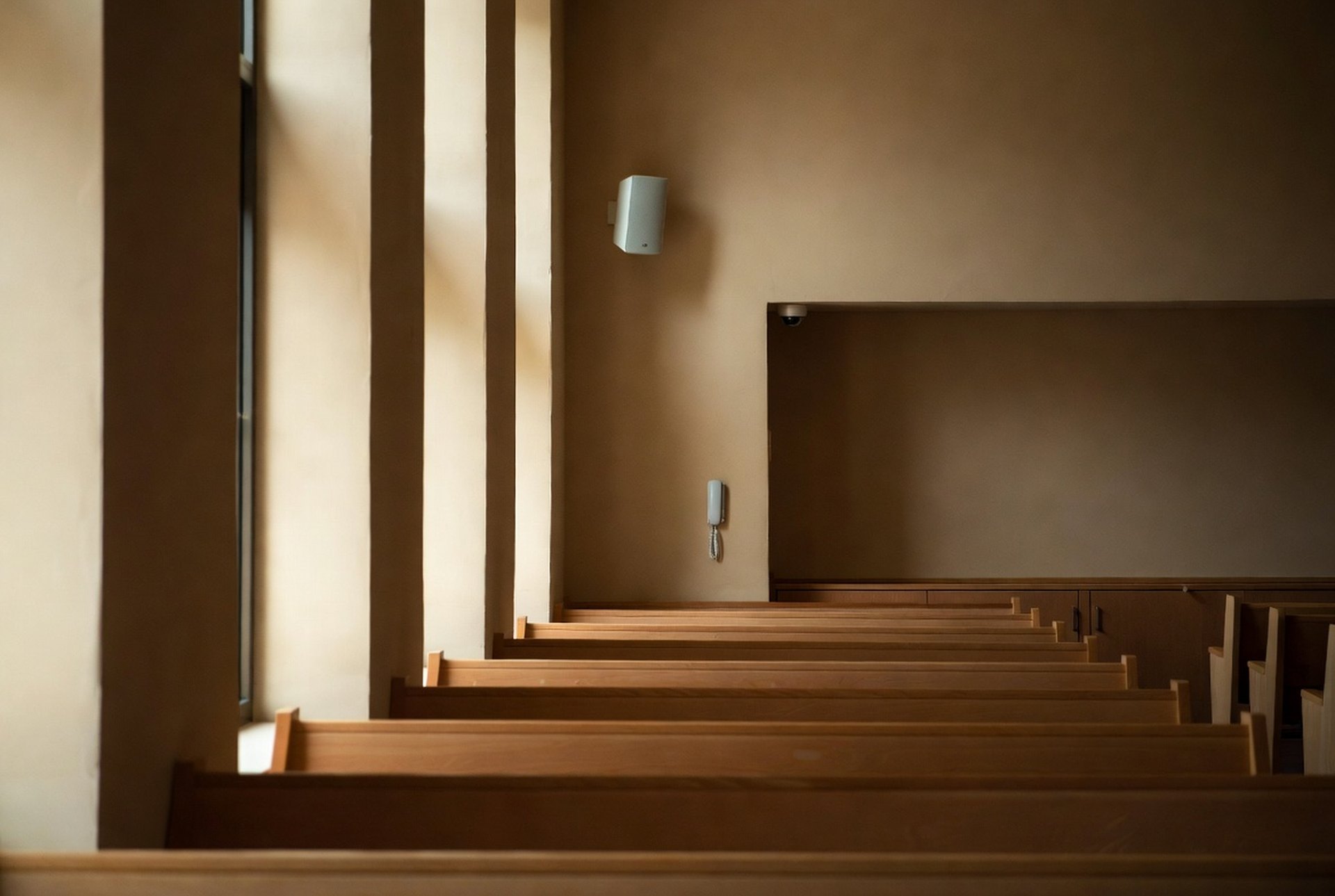An empty house-of-worship interior with rows of wooden seating and a wall-mounted speaker